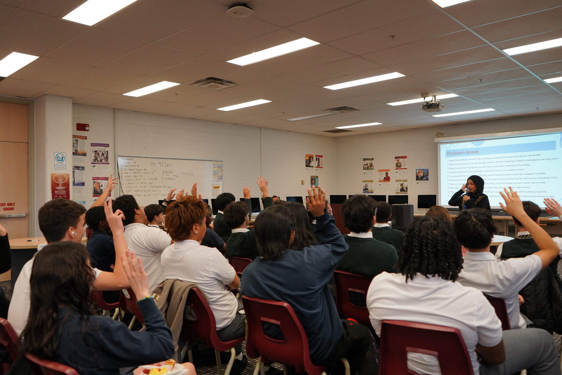 Meena presenting to students with hands raised in a classroom